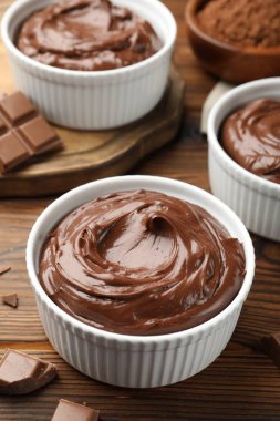 Tabaklardaki lezzetli pudingler ve ahşap masadaki çikolata parçaları, yakın plan.