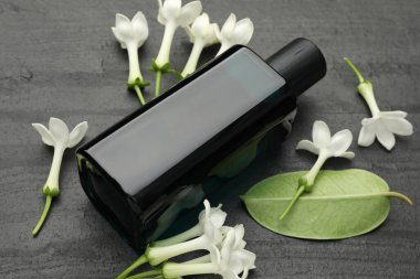 Parfüm, yasemin çiçekleri ve yeşil yaprak siyah masada, yakın plan.