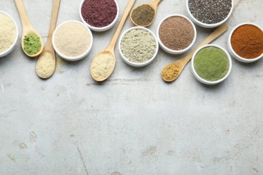 Farklı süper yiyecek tozları, gri desenli masa üzerinde kaşık ve kâseler halinde düz uzanıyordu. Metin için boşluk