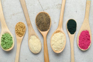 Gri desenli masa üzerinde kaşık içinde farklı süper yiyecek tozları.