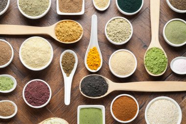 Tabaklardaki farklı süper yiyecek tozları ve tahta masa üzerindeki kaşıklar.