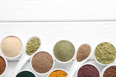 Kâselerdeki farklı süper yiyecek tozları ve beyaz ahşap masa üzerindeki kaşıklar düz yatıyordu. Metin için boşluk