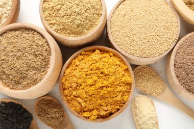 Farklı süper yiyecek tozları kaseler ve beyaz arka planda kaşıklar, düz yatış