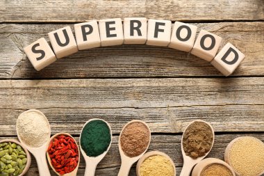 Farklı süper yiyecek tozları ve tahta masadaki küplerden yapılmış sözcükler.