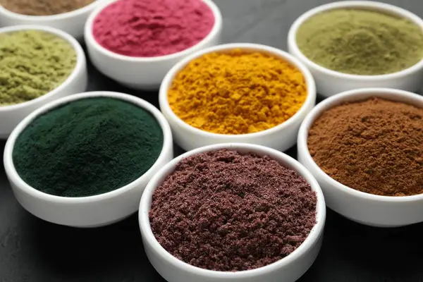 Karanlık masadaki kaselerde farklı süper yiyecek tozları, yakın plan.