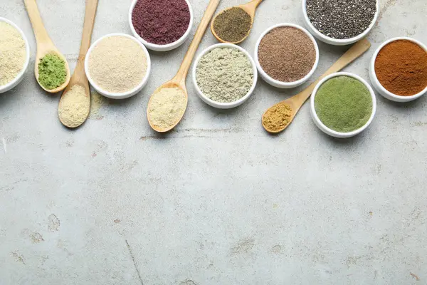 Farklı süper yiyecek tozları, gri desenli masa üzerinde kaşık ve kâseler halinde düz uzanıyordu. Metin için boşluk