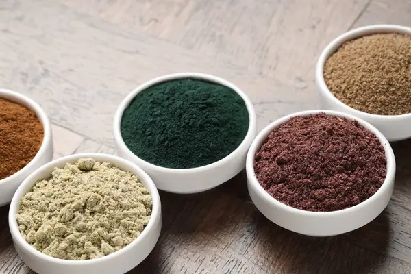 Tahta masadaki kaselerde farklı süper yiyecek tozları, yakın plan.