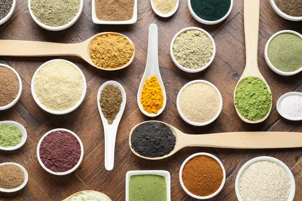 Tabaklardaki farklı süper yiyecek tozları ve tahta masa üzerindeki kaşıklar.