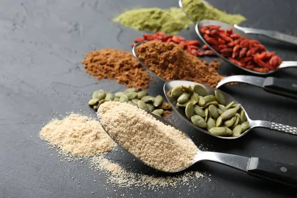 Siyah masadaki kaşıklardaki farklı süper yiyecekler, yakın plan. Metin için boşluk