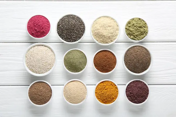 Beyaz ahşap masadaki kaselerdeki farklı süper yiyecek tozları.