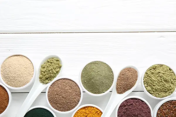 Kâselerdeki farklı süper yiyecek tozları ve beyaz ahşap masa üzerindeki kaşıklar düz yatıyordu. Metin için boşluk