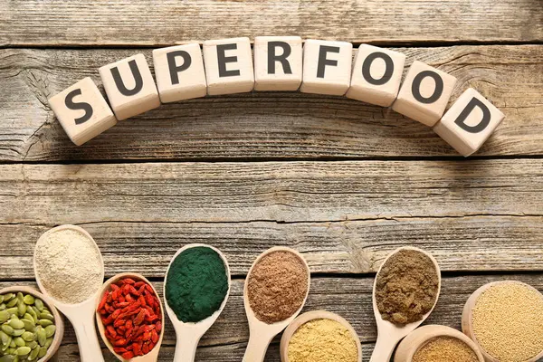 Farklı süper yiyecek tozları ve tahta masadaki küplerden yapılmış sözcükler.