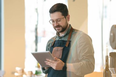 Kahvesinde tabletle çalışan gülümseyen bir işletme sahibi.