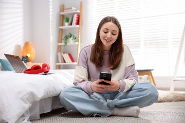 Genç kız evde yerde akıllı telefon kullanıyor.
