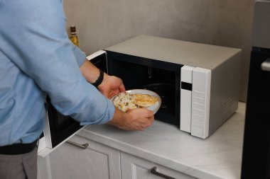 Yemek tabağını mikrodalgaya koyan adam, yakın plan.