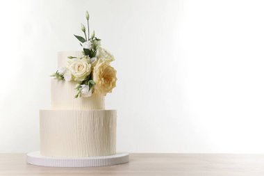Ahşap masadaki çiçeklerle süslenmiş nefis düğün pastası beyaz arka planda. Metin için boşluk