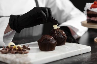 Mutfaktaki siyah mermer masada lezzetli çikolatalı kekler dekore eden şekerci, yakın plan.