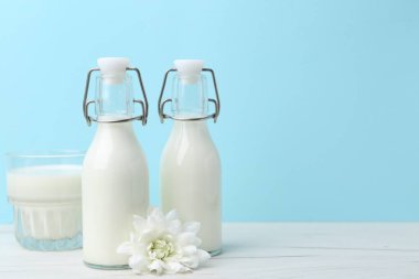 Açık mavi arka planda beyaz masada taze süt ve çiçek. Metin için boşluk