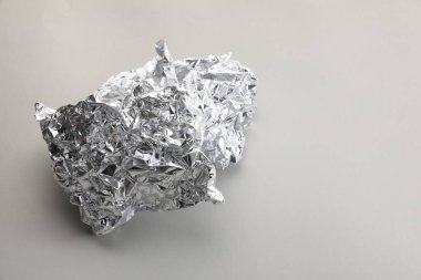 Açık gri arka planda buruşmuş alüminyum folyo parçası, yakın plan. Metin için boşluk