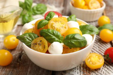 Sarı domatesli taze salata, fesleğen ve ahşap masada mozzarella peyniri, yakın plan.