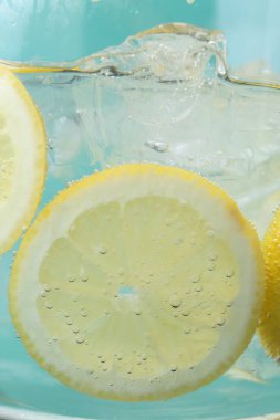 Açık mavi arka planda limon dilimleri ve buzla soda tazeleniyor. Yakın plan.