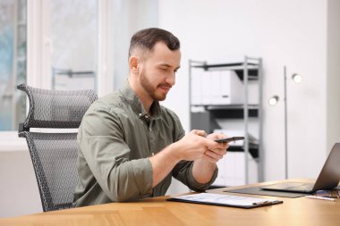 Ofisteki masada akıllı telefondaki tarama uygulamasını kullanarak belgenin fotoğrafını çeken bir adam.