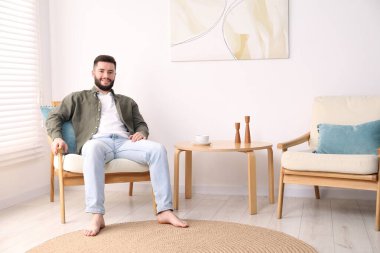 Gülümseyen adam evdeki koltukta dinleniyor.