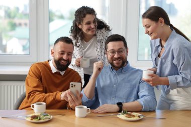 Ofiste öğle arasında iş arkadaşlarına akıllı telefondan bir şey gösteren bir adam.