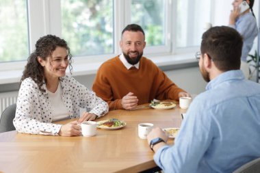 İş arkadaşları ofiste yemek yiyor ve sohbet ediyorlar.