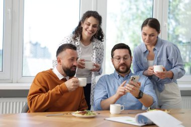 Ofiste öğle arasında iş arkadaşlarına akıllı telefondan bir şey gösteren bir adam.
