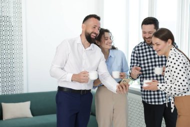 Ofisteki kahve molasında iş arkadaşlarına telefonunda bir şey gösteren bir adam.