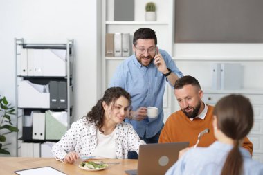 İş arkadaşları ofiste yemek yiyor ve sohbet ediyorlar.