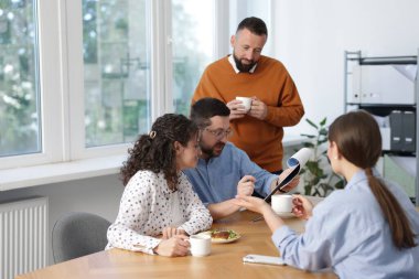 İş arkadaşları yemek yiyor ve ofiste öğle arasında iş tartışıyorlar.