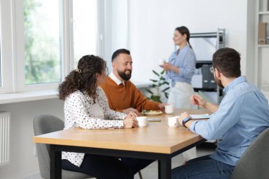 İş arkadaşları ofiste yemek yiyor ve sohbet ediyorlar.