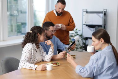 İş arkadaşları yemek yiyor ve ofiste öğle arasında iş tartışıyorlar.