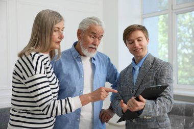 Gülümseyen bir emlakçı pano ile evde çiftlerle çalışıyor.