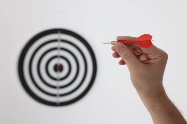 Hedef alınıyor. Oklu bir adam arka planda dart tahtasına nişan alıyor, yakın plan.