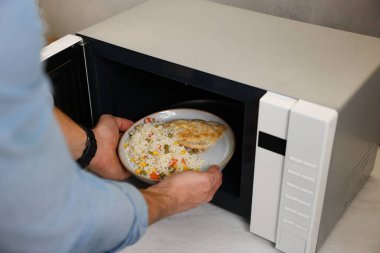 Yemek tabağını mikrodalgaya koyan adam, yakın plan.