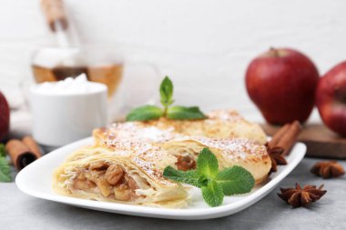 Açık gri masada pudra şekeri, nane ve baharatla lezzetli elmalı turtalar, yakın plan.