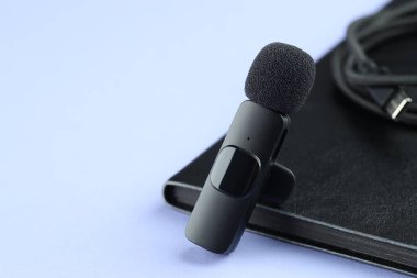 Lavalier mikrofon, kablo ve defter açık mavi arka planda, yakın plan. Metin için boşluk