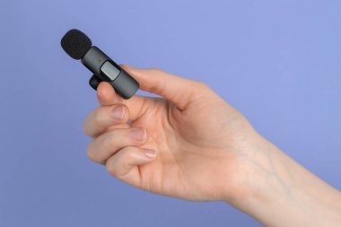 Açık mavi arka planda lavalier mikrofon tutan kadın, yakın plan.