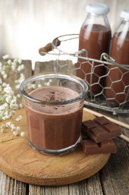 Lezzetli çikolatalı süt, talaş, parça ve çiçekler ahşap masada.