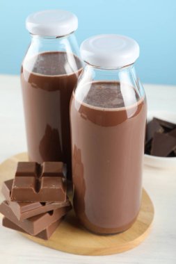 Lezzetli çikolatalı süt ve parçalar beyaz masada açık mavi arka planda, yakın plan