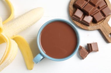 Lezzetli çikolatalı süt, parçalar ve muz beyaz ahşap masada, düz uzanmış