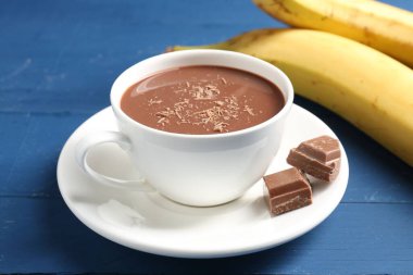 Lezzetli çikolatalı süt, parçalar ve muzlar mavi ahşap masada, yakın plan