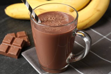 Cam bardakta lezzetli çikolatalı süt, siyah masada parçalar ve muzlar, yakın plan.