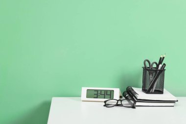 Kırtasiyeli şık bir iş yeri ve açık yeşil duvarın yanındaki beyaz masadaki saat. Metin için boşluk