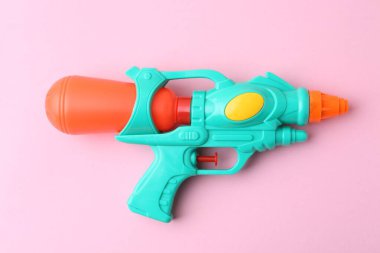 Açık pembe zemin üzerinde parlak plastik su tabancası, üst görünüm