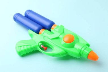 Açık mavi arkaplanda parlak plastik su tabancası, yakın plan.