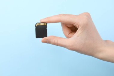 Hafıza kartını açık mavi arkaplanda tutan kadın, yakın plan